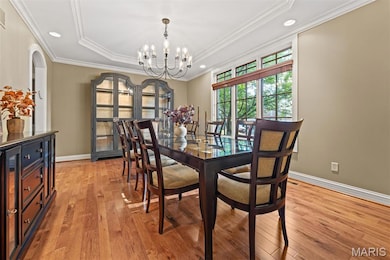 Dining room with a raised ceiling, light wood finished floors, a chandelier, crown molding, and recessed lighting