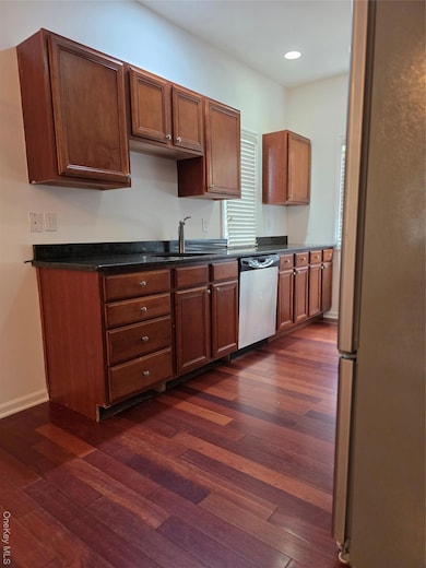 Kitchen with refrigerator, dark wood-style floors, dark countertops, dishwasher, and recessed lighting