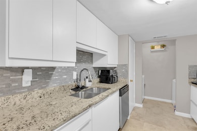 Kitchen featuring tasteful backsplash, white cabinetry, light stone countertops, and light tile patterned floors