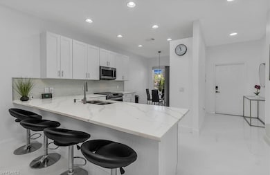 Kitchen with tasteful backsplash, light stone counters, a breakfast bar, white cabinetry, and recessed lighting