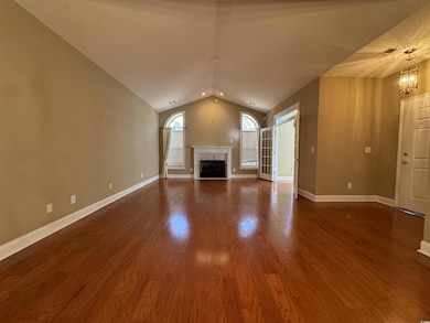 Unfurnished living room with lofted ceiling, a high end fireplace, dark wood finished floors, baseboards, and a chandelier