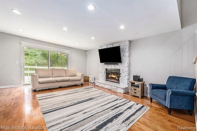 Living area with a stone fireplace, light wood-style floors, and recessed lighting
