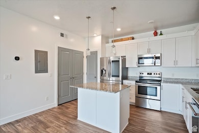 Kitchen featuring stainless steel appliances, a center island, light stone counters, dark wood finished floors, and recessed lighting