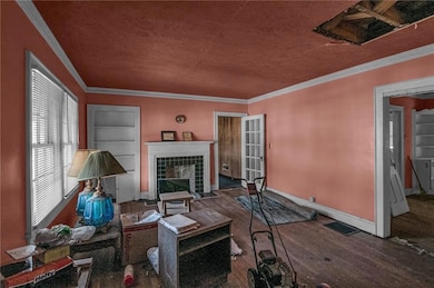 Living room with dark wood-type flooring, a textured ceiling, ornamental molding, built in features, and a tiled fireplace