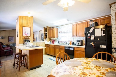 Kitchen featuring light countertops, a kitchen bar, black appliances, brown cabinetry, and a textured ceiling