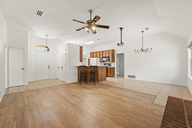 Unfurnished living room featuring ceiling fan with notable chandelier, lofted ceiling, and light hardwood / wood-style floors