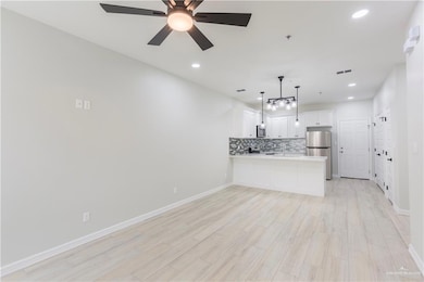Kitchen featuring white cabinets, ceiling fan, stainless steel appliances, pendant lighting, and kitchen peninsula