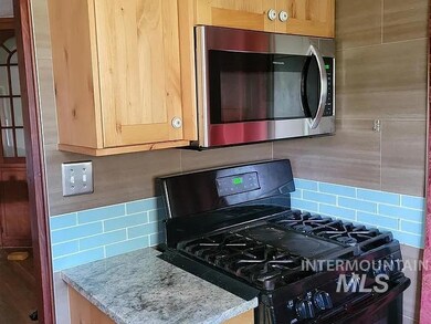Kitchen view of black range with gas cooktop, stainless steel microwave, decorative backsplash, and light stone counters