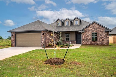 View of front facade featuring covered porch, a shingled roof, brick siding, an attached garage, and driveway