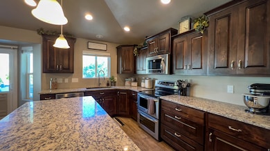 Kitchen featuring dark brown cabinetry, appliances with stainless steel finishes, decorative light fixtures, recessed lighting, and light stone counters