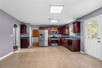 Kitchen featuring appliances with stainless steel finishes, arched walkways, dark brown cabinets, dark countertops, and tasteful backsplash