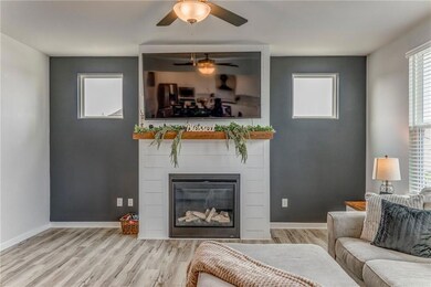 Living room with wood finished floors, a ceiling fan, a glass covered fireplace, and baseboards