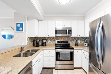Kitchen with stainless steel appliances, a sink, ornamental molding, backsplash, and white cabinets