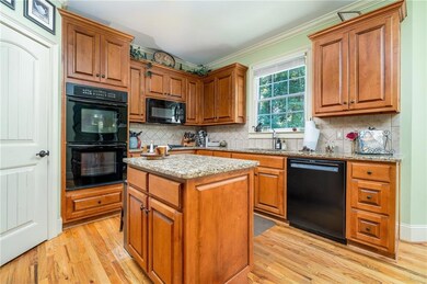 Kitchen with black appliances, light wood-style floors, light stone counters, ornamental molding, and brown cabinets