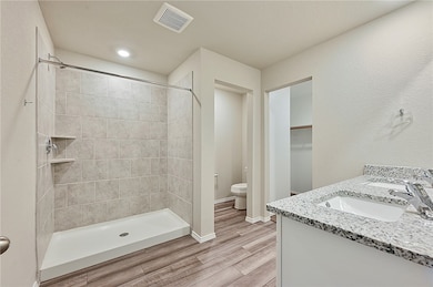 Bathroom with double vanity, a stall shower, light wood finished floors, and a walk in closet