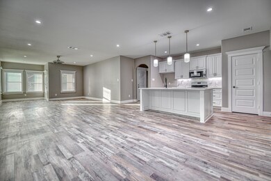 Kitchen featuring arched walkways, open floor plan, white cabinets, a kitchen island with sink, and recessed lighting