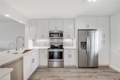 Kitchen with appliances with stainless steel finishes, a sink, tasteful backsplash, white cabinetry, and light wood-type flooring