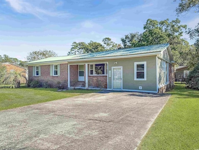 View of front facade with a front yard, brick siding, a metal roof, a porch, and concrete driveway