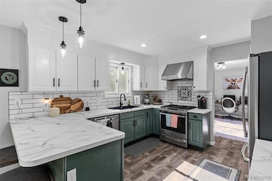 Kitchen featuring green cabinets, decorative light fixtures, white cabinetry, appliances with stainless steel finishes, and a peninsula