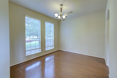 This room features hardwood flooring, large windows with blinds allowing natural light, neutral wall colors, and a modern overhead light fixture, creating a bright and welcoming space.