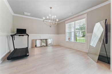 Spacious DR seats 12 featuring ornamental molding, a chandelier, a wainscoted wall, a decorative wall, and light wood finished floors