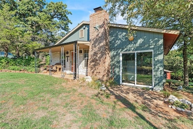 Back of property featuring a chimney, a porch, a lawn, and brick siding