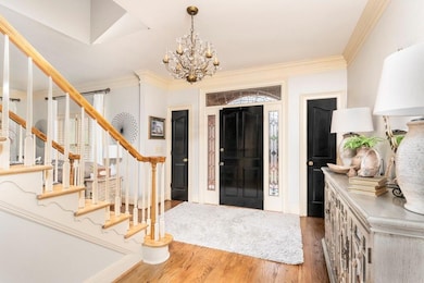Entrance foyer featuring stairway, a chandelier, wood finished floors, and ornamental molding