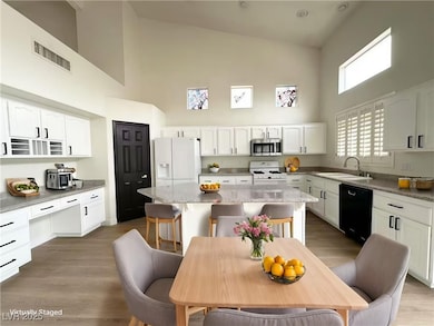 Kitchen featuring high vaulted ceiling, white cabinets, white appliances, dark wood-type flooring, and light stone countertops