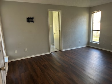 Empty room with a textured wall, dark wood-type flooring, and a textured ceiling