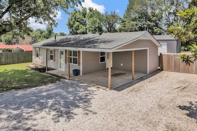 View of front of home with a fenced backyard, a shingled roof, an attached carport, and gravel driveway
