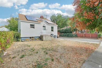 Back of house with solar panels, a chimney, and roof with shingles