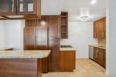 Kitchen featuring light stone countertops, appliances with stainless steel finishes, decorative backsplash, brown cabinetry, and glass insert cabinets
