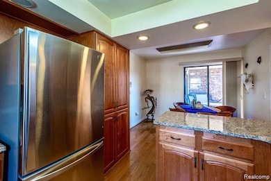 Kitchen featuring freestanding refrigerator, recessed lighting, light stone countertops, light wood-style floors, and brown cabinetry