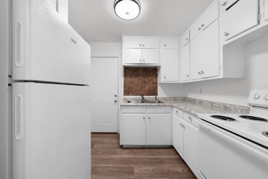 Kitchen with white appliances, dark wood-style flooring, light countertops, and white cabinets