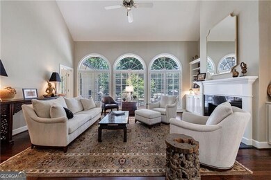 Living room with wood finished floors, a glass covered fireplace, a ceiling fan, and high vaulted ceiling