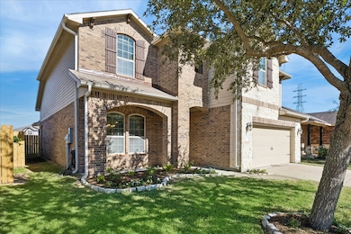 This inviting two-story brick home features a charming exterior with arched windows, a well-kept lawn, and a spacious two-car garage. A mature tree adds character and shade to the front yard.