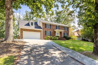 Colonial inspired home featuring a front lawn, concrete driveway, brick siding, an attached garage, and a shingled roof