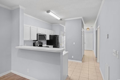 Kitchen with white cabinets, ornamental molding, light countertops, a peninsula, and a textured ceiling