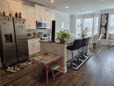 Kitchen featuring appliances with stainless steel finishes, crown molding, dark wood finished floors, a kitchen island with sink, and recessed lighting