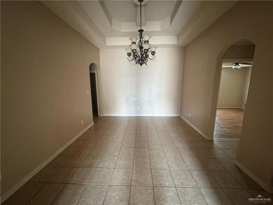 Tiled spare room with arched walkways, a tray ceiling, a chandelier, ceiling fan, and baseboards