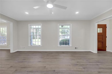 Empty room featuring ornamental molding, healthy amount of natural light, wood finished floors, a ceiling fan, and baseboards