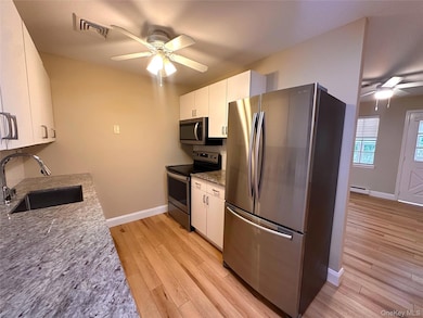 Kitchen featuring a ceiling fan, appliances with stainless steel finishes, light stone counters, and white cabinetry