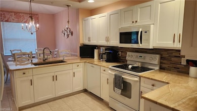 Kitchen featuring white appliances, tasteful backsplash, a peninsula, light tile patterned flooring, and decorative light fixtures