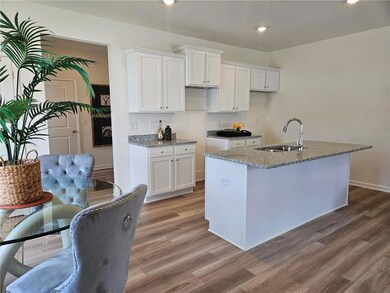 Kitchen featuring a kitchen island with sink, white cabinetry, light stone counters, wood finished floors, and recessed lighting
