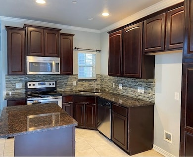 Kitchen with dark stone countertops, appliances with stainless steel finishes, crown molding, dark brown cabinets, and tasteful backsplash