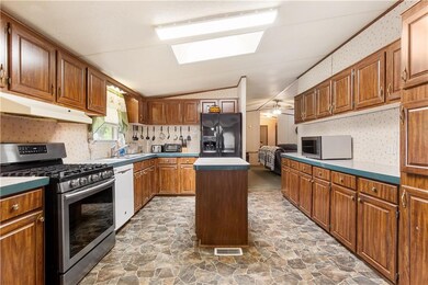 Kitchen featuring stainless steel appliances, under cabinet range hood, wallpapered walls, stone flooring, and a center island