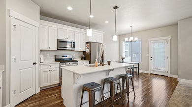 Kitchen with appliances with stainless steel finishes, a kitchen breakfast bar, a kitchen island with sink, decorative light fixtures, and white cabinetry