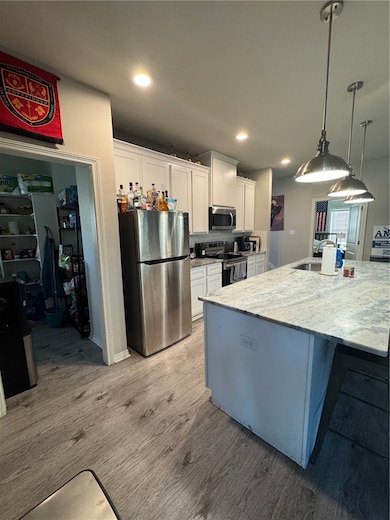 Kitchen featuring white cabinetry, stainless steel appliances, decorative light fixtures, light wood finished floors, and light stone counters