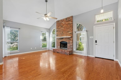 Living room with high vaulted ceiling, a brick fireplace, hardwood flooring, and ceiling fan.