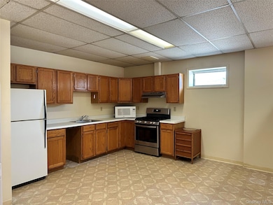 Kitchen with white appliances, light countertops, brown cabinetry, and a paneled ceiling